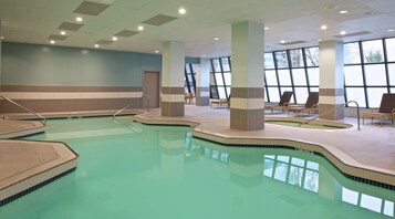 Piscina interna com bordas azulejadas, cadeiras de descanso e grandes janelas que permitem entrada de luz natural.
