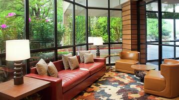 A modern lobby with a leather sofa, armchairs, a patterned rug, and large windows offering a view of greenery.