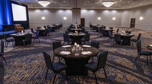 A conference room with multiple tables and chairs, a large screen, and chandeliers. - Embassy Suites by Hilton Portland Tigard (Tigard)