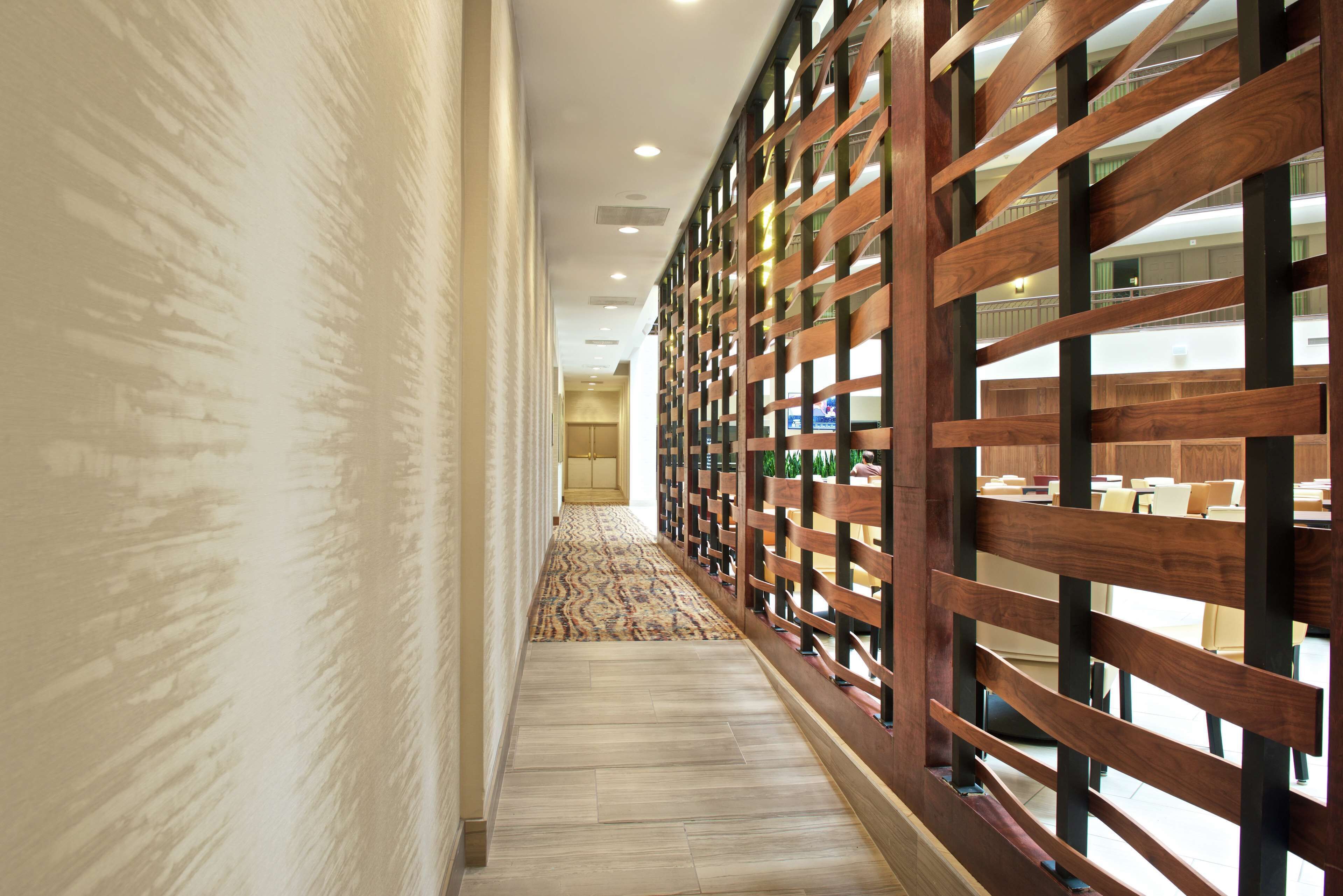 A corridor with a patterned carpet, wooden paneling, and a view of a dining area with tables and chairs.