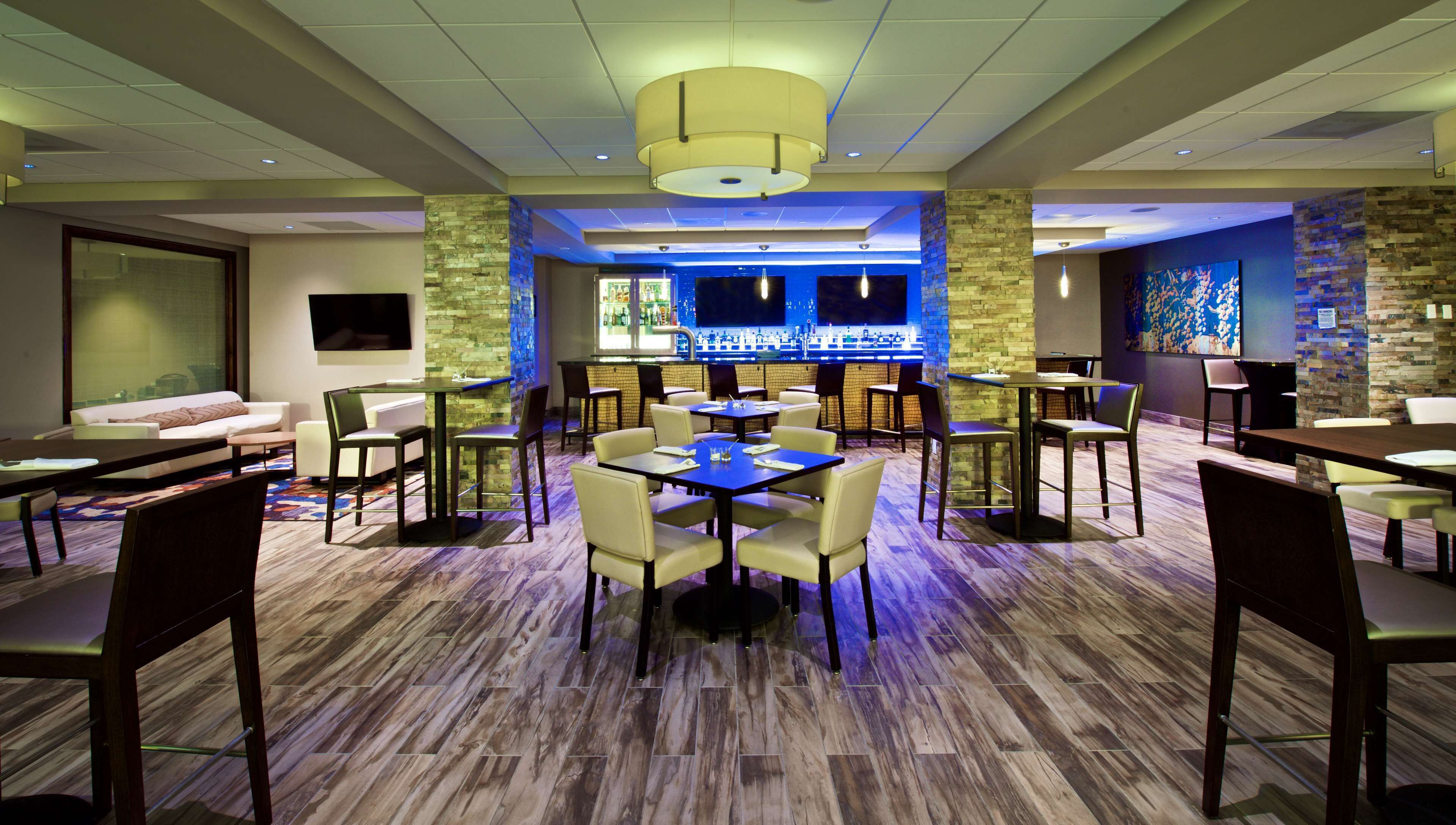 A modern hotel lobby with a bar area, seating arrangements, and a television screen.