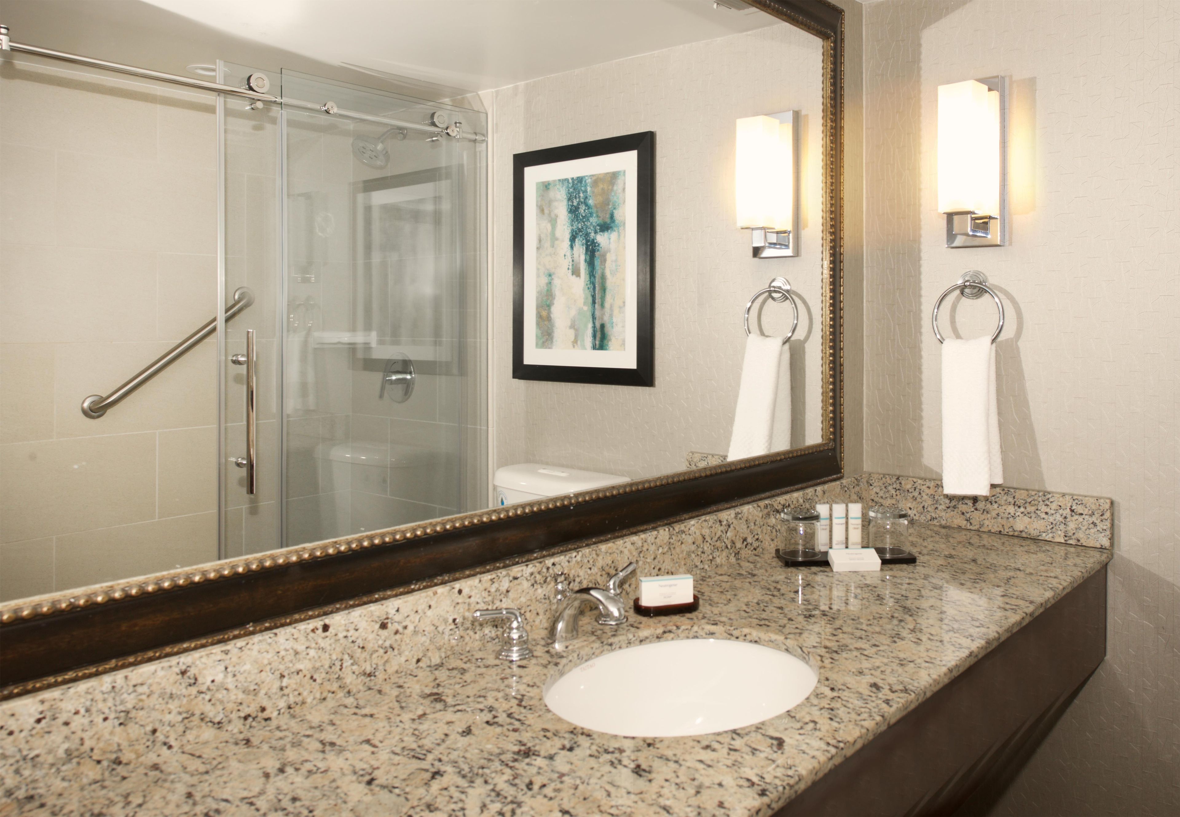 Un baño con cabina de ducha de vidrio, un lavamanos con encimera de granito y un espejo grande con un marco decorativo.