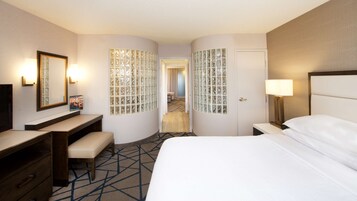 Quarto de hotel com cama, escrivaninha, cadeira, espelho e porta.