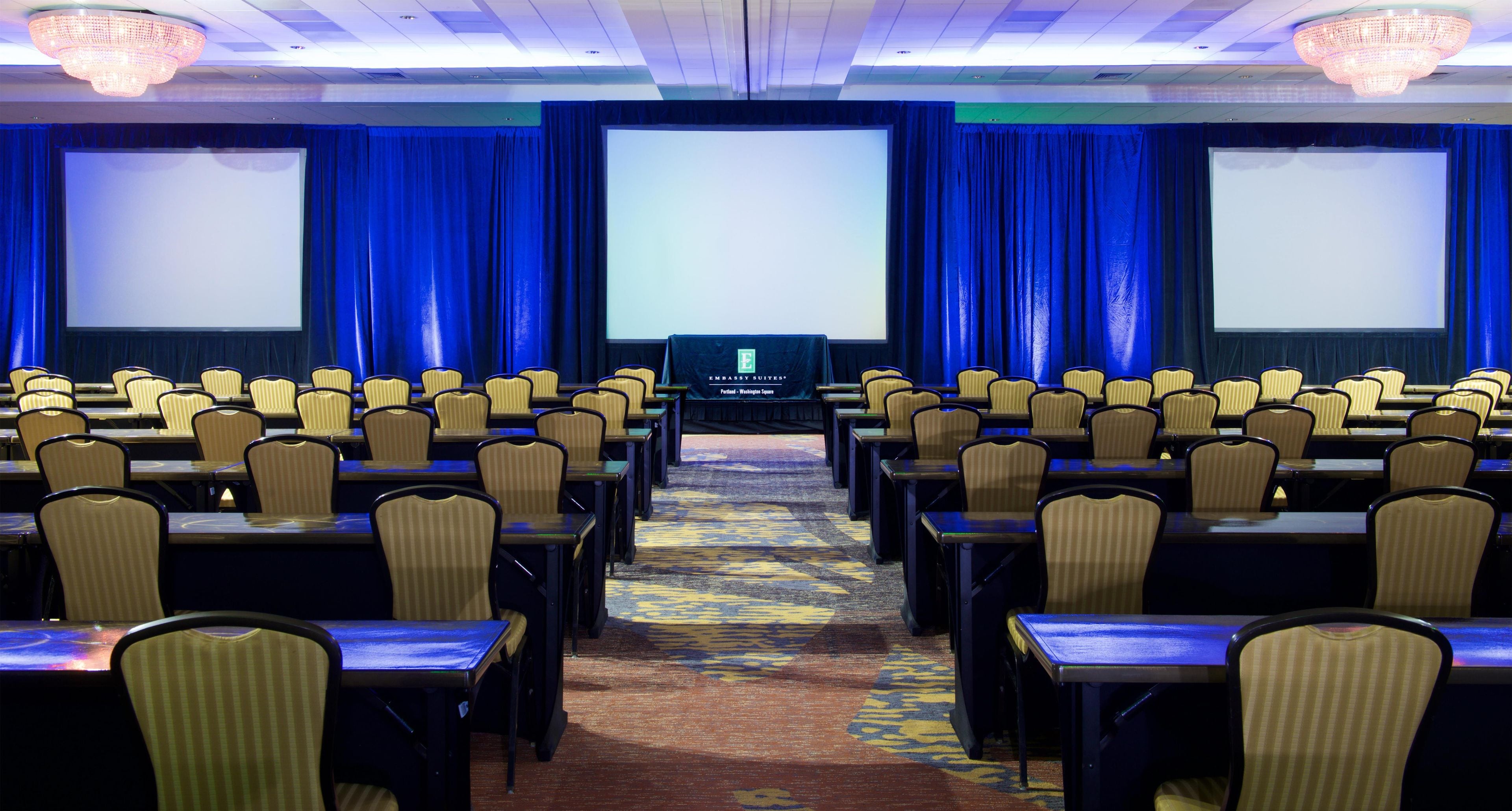 A conference room with rows of chairs, a stage with a screen, and a carpeted floor.
