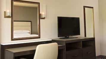 Habitació d'hotel amb llit, televisió, escriptori i una cadira, i un mirall.