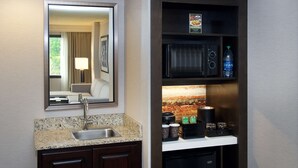 A hotel bathroom with a sink, mirror, and a shelf with a microwave, coffee maker, and tea. - Embassy Suites by Hilton Portland Tigard (Tigard)