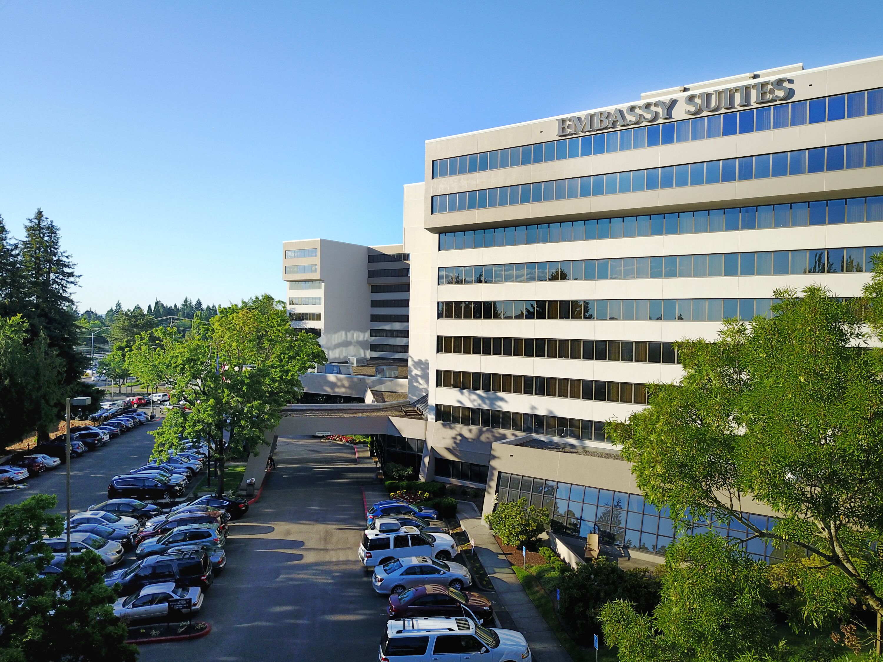 A modern building with "EMBASSY SUITES" signage, surrounded by a parking lot and greenery.