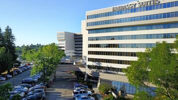 A modern building with "EMBASSY SUITES" signage, surrounded by a parking lot and greenery.