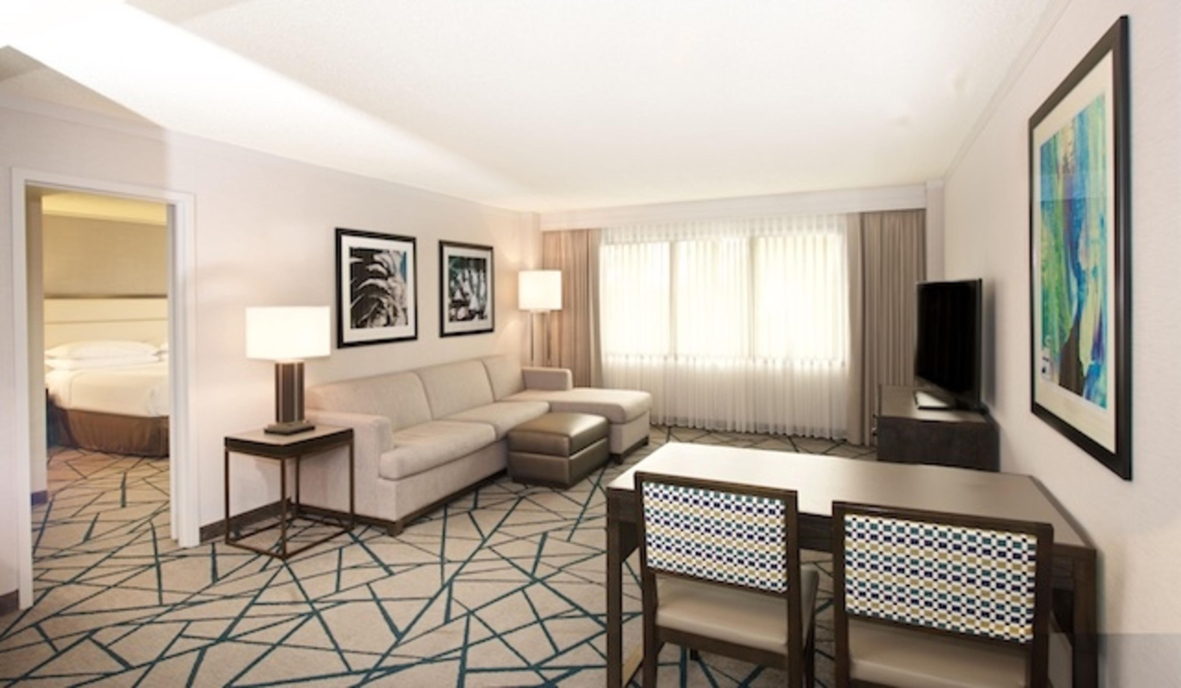 Habitación de hotel con sofá, dos sillones, televisor y mesa de comedor.