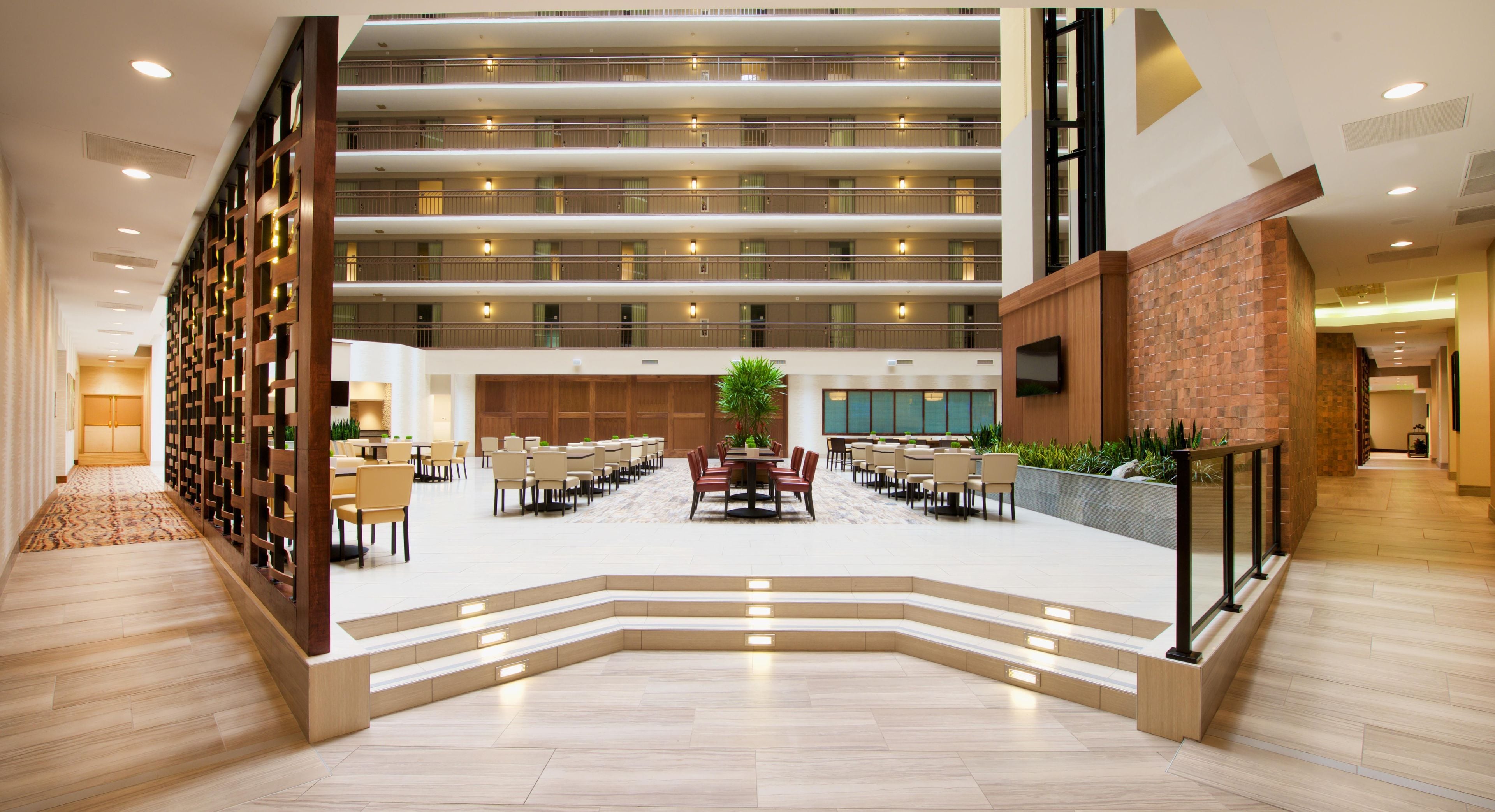 A multi-level hotel lobby with a central seating area, a staircase, and a high ceiling.