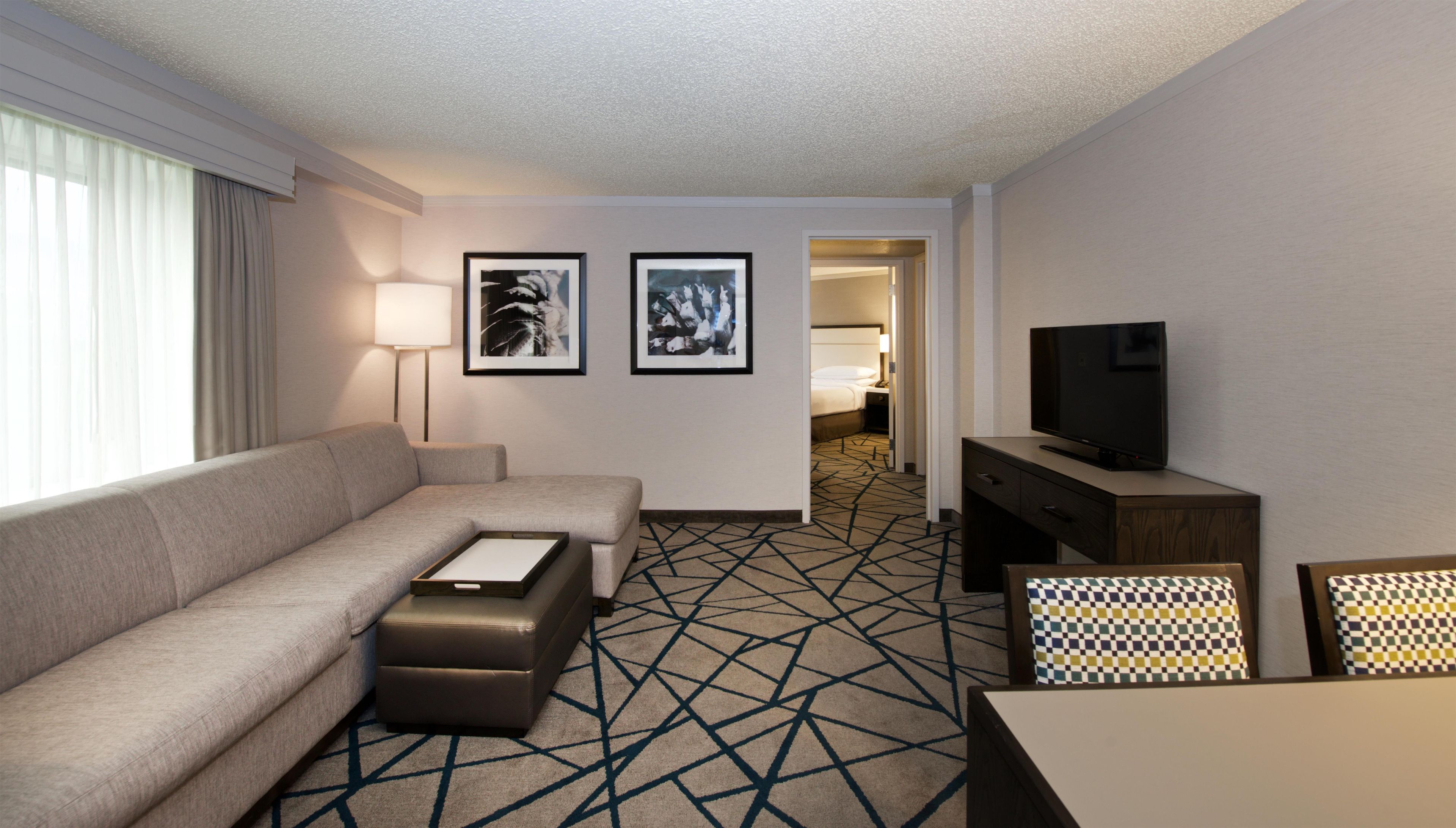 A hotel room with a sofa, a television, a desk, and two framed pictures on the wall.