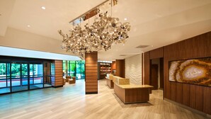 A modern hotel lobby with a wooden reception desk, a large decorative chandelier, and a view of the outdoors through large windows. - Embassy Suites by Hilton Portland Tigard (Tigard)