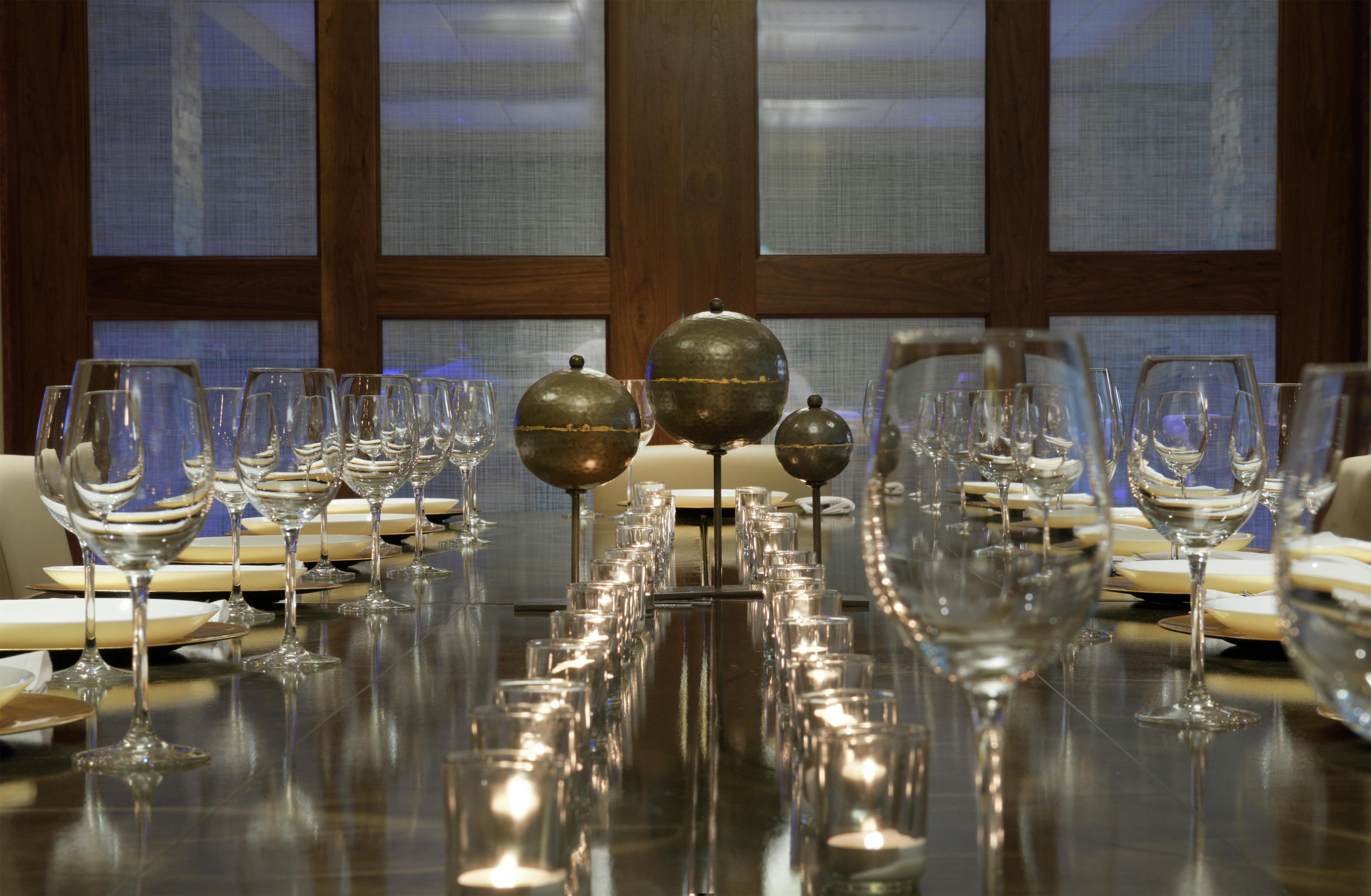 A dining table set with multiple wine glasses and plates, reflecting on the polished surface.