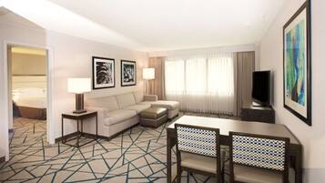 Una habitación de hotel con sofá, dos sillones, televisor y una mesa de comedor con sillas.