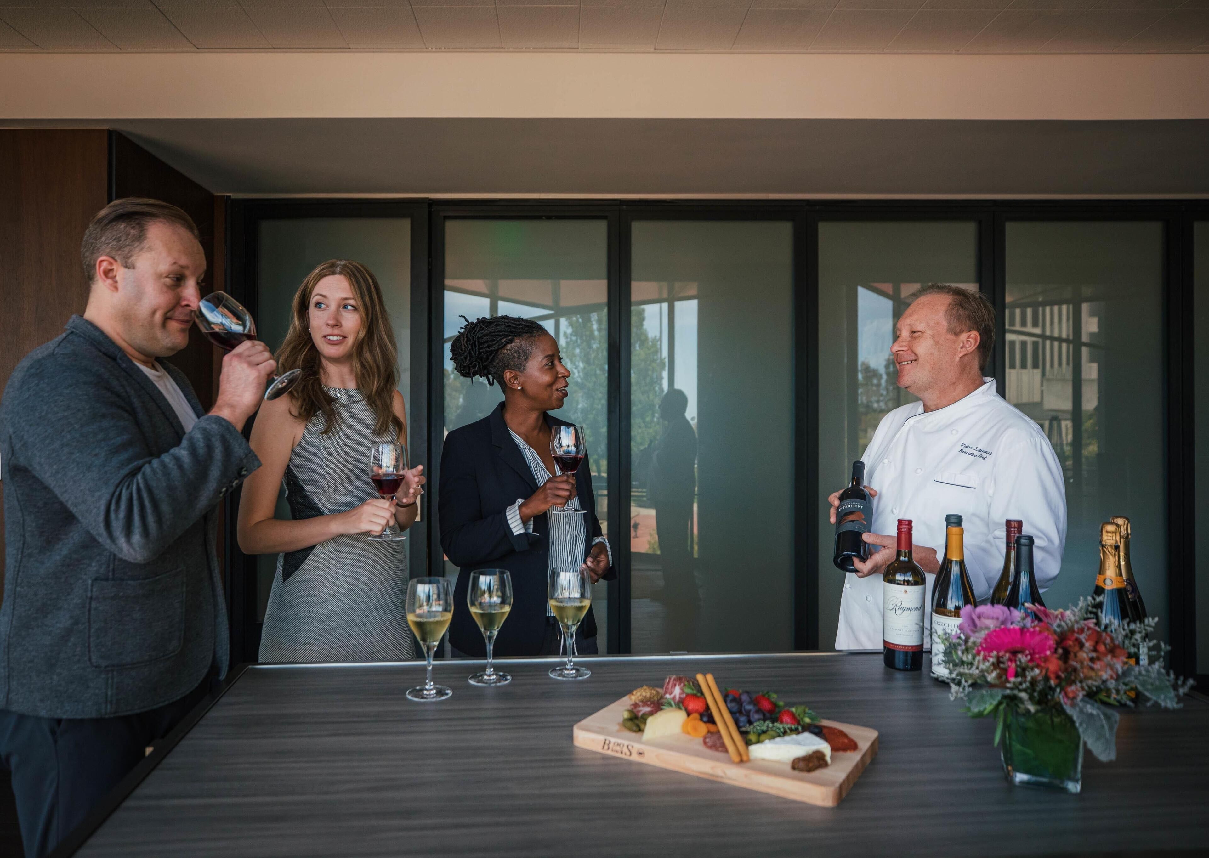 A group of people standing around a table with wine bottles and a charcuterie board.