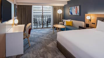 A hotel room with a bed, a desk, a chair, a small table, a sofa, and a TV.