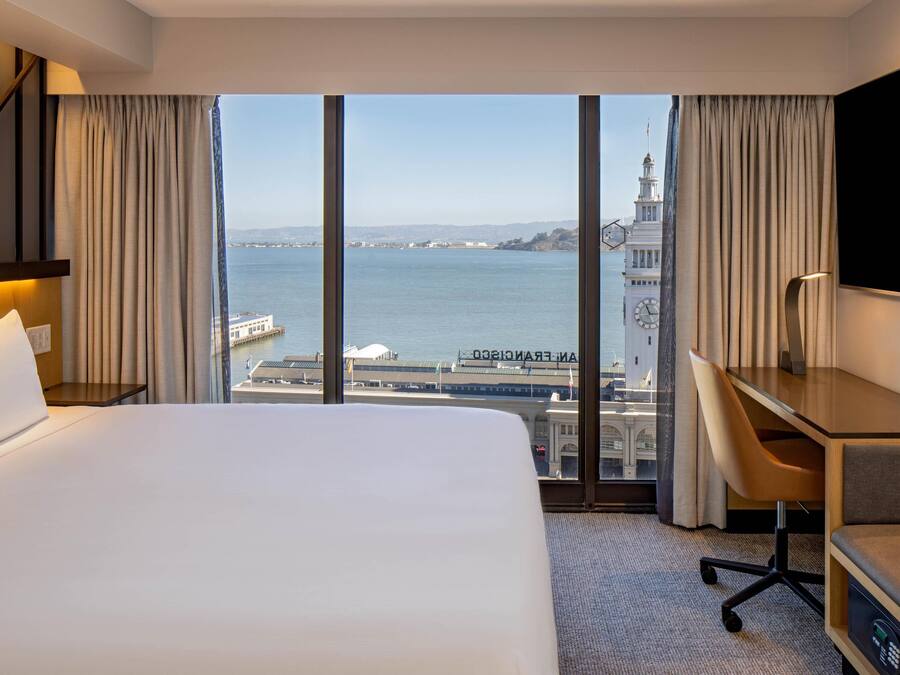 Habitación de hotel con una cama grande, un escritorio y vistas al agua y una torre del reloj.