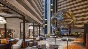 Spaziosa hall con sedute moderne, una grande scultura astratta e un soffitto alto illuminato da luci lineari.