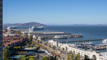 Un paisaje costero con un gran crucero atracado en el puerto, un edificio blanco destacado con una entrada arqueada, y una vista despejada del océano y colinas distantes.