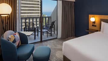 A hotel room with a bed, a desk, a chair, a small table, and a view of the outdoors.
