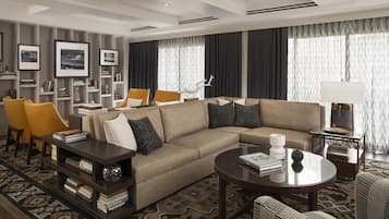 A modern living room with a sectional sofa, two armchairs, a coffee table, a bookshelf, and a large window with curtains.