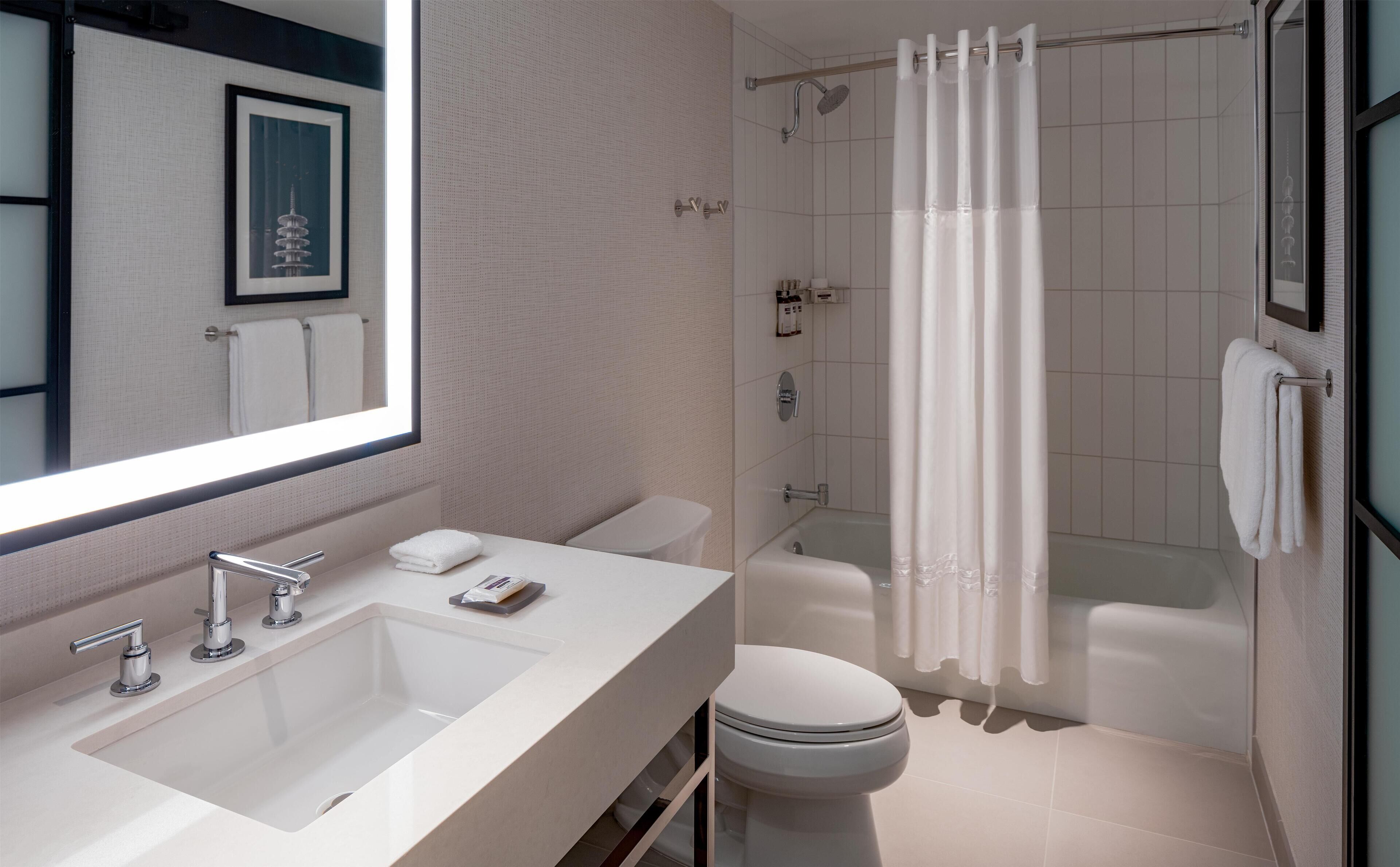 A modern bathroom with a large mirror, a sink, a toilet, and a shower with a curtain.