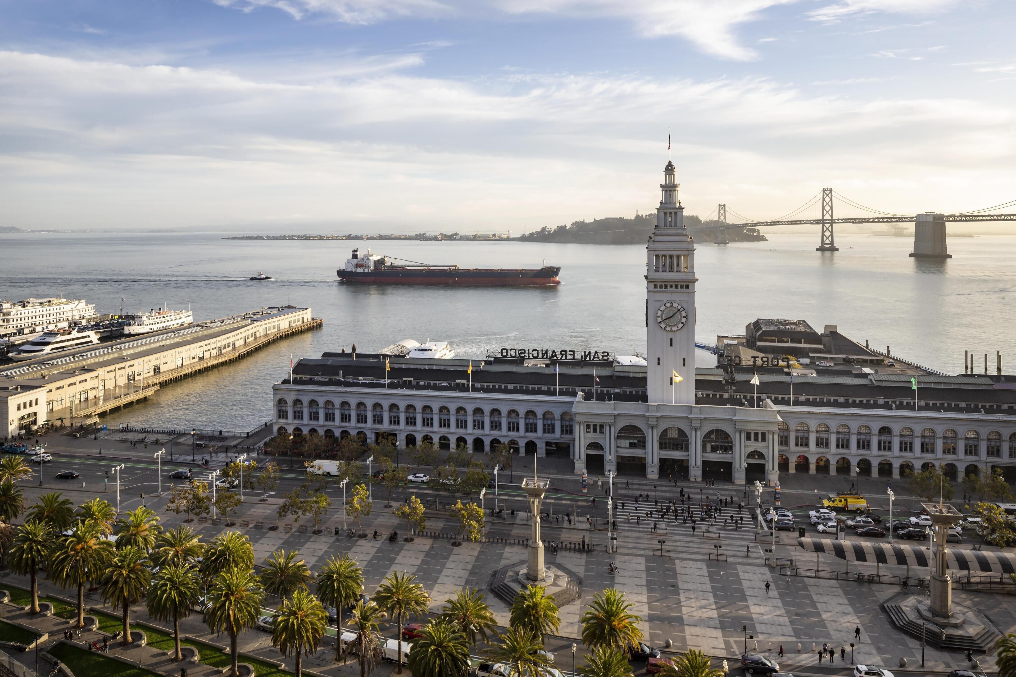Un grande edificio con una torre dell'orologio, un lungomare e un ponte sullo sfondo.