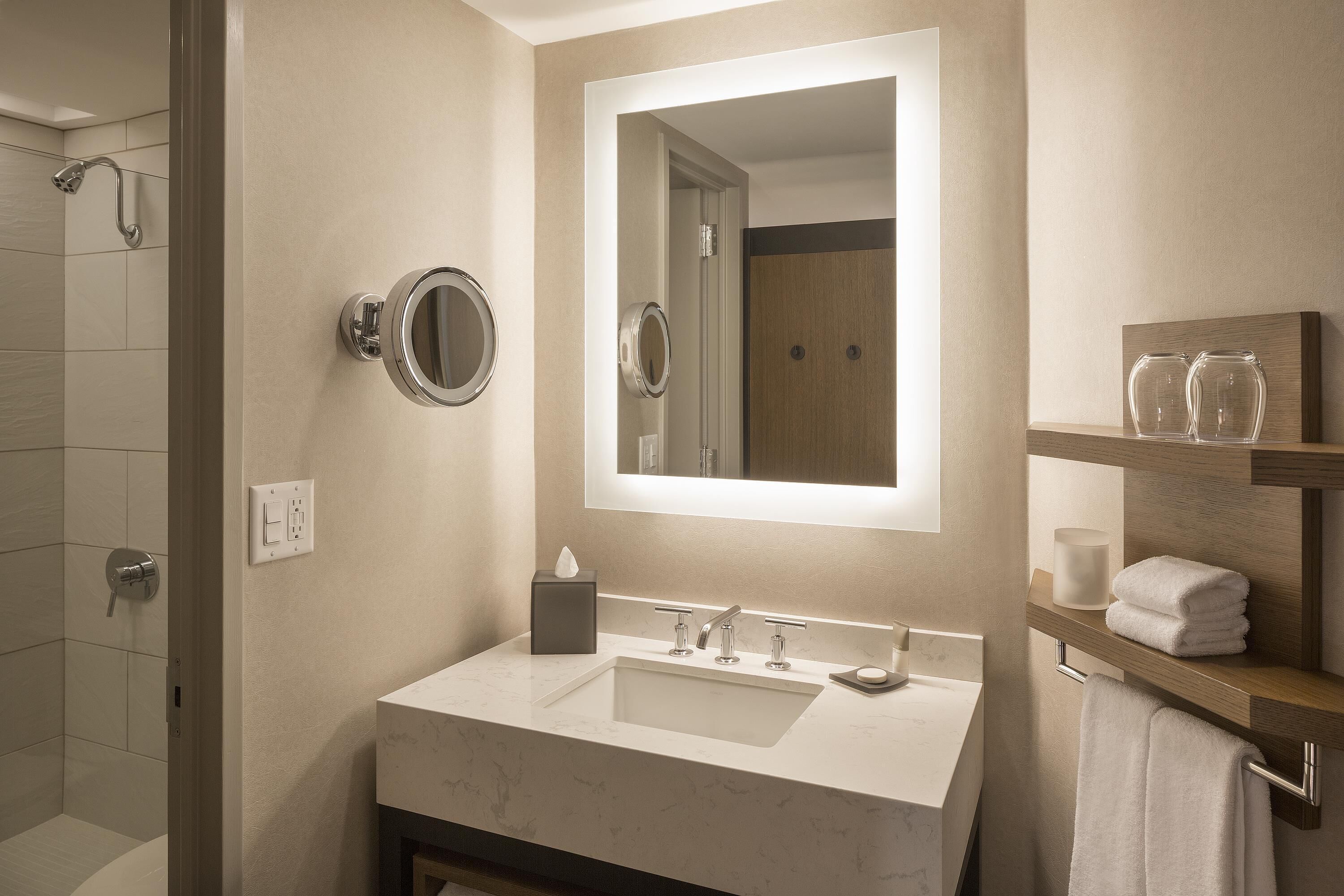 A modern bathroom with a large mirror, a sink, and a shower.