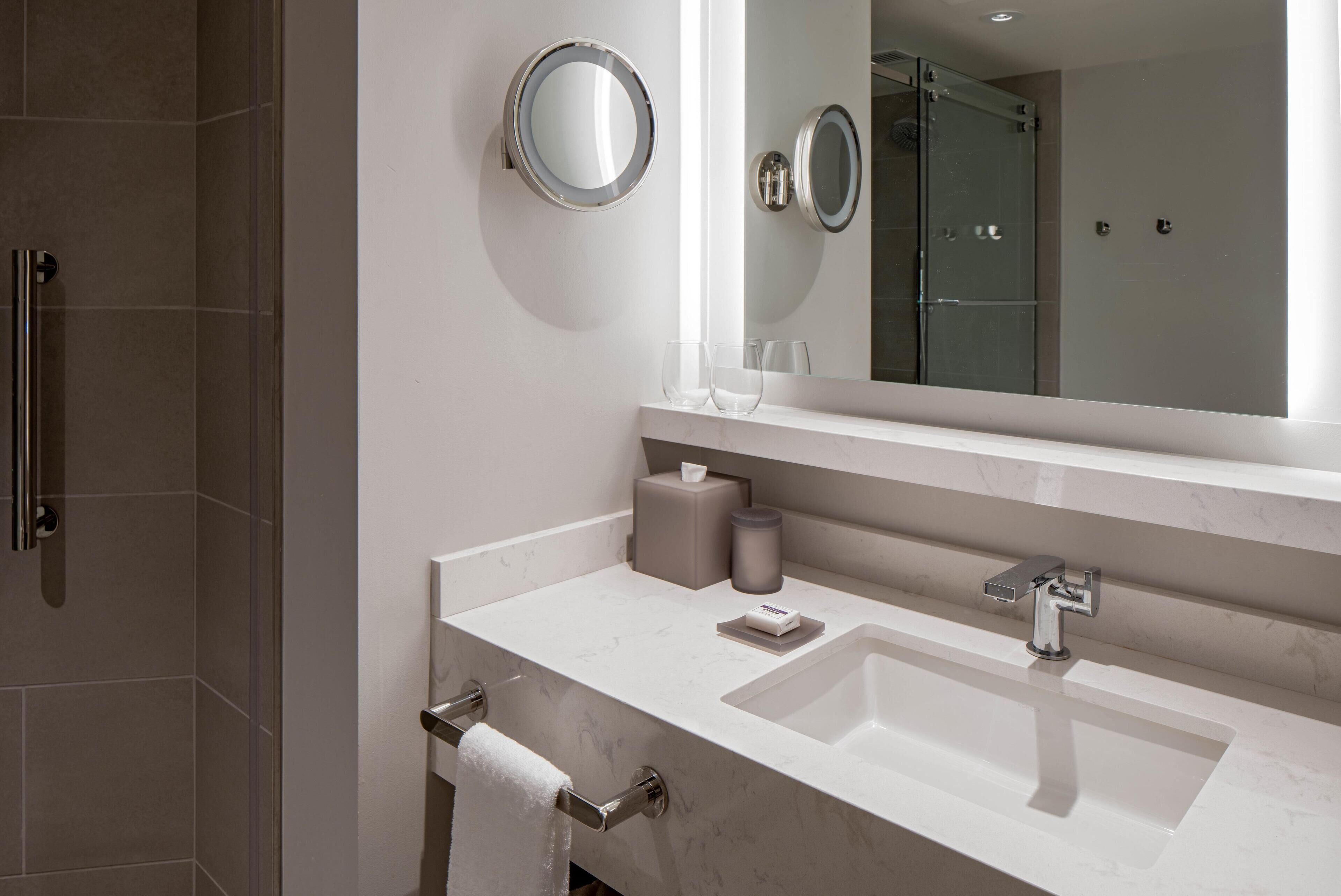 A modern bathroom with a large mirror, a sink, and a glass shower enclosure.