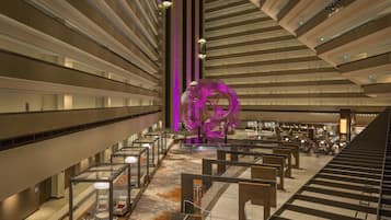 A spacious hotel lobby with a central staircase, seating areas, and a distinctive purple sculpture.