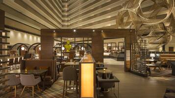 Un moderno vestíbulo de hotel con bar central, zonas de estar y una escultura distintiva en el techo.