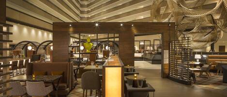 A modern hotel lobby with a central bar, seating areas, and a distinctive ceiling sculpture.