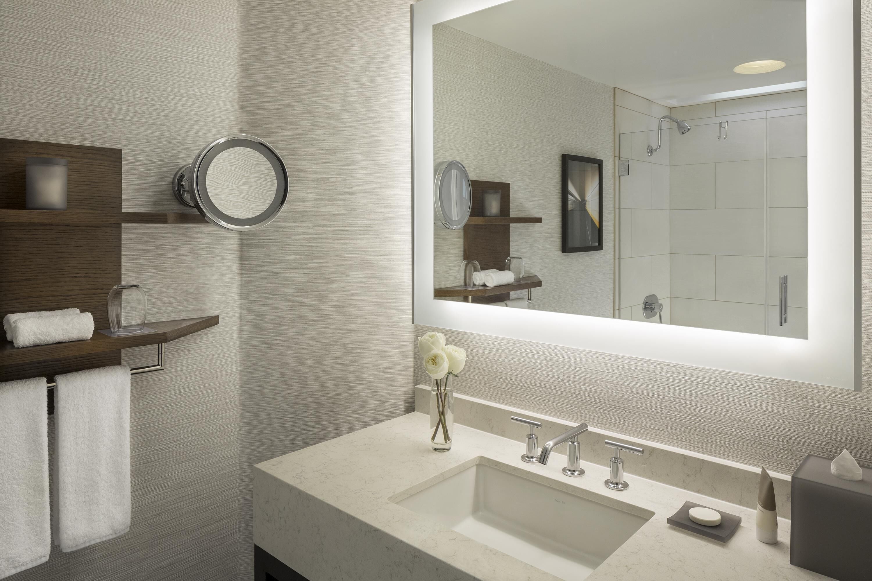 Ein modernes Badezimmer mit großem Spiegel, Waschbecken, Dusche und Handtuchhalter.