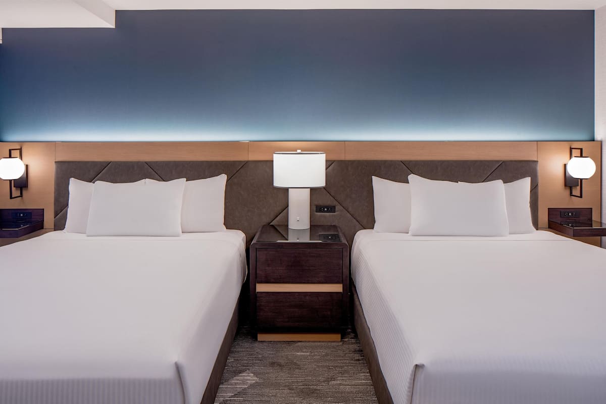 Una camera d'hotel con due letti, un comodino tra di essi, una lampada a parete e un'ampia parete sopra i letti.