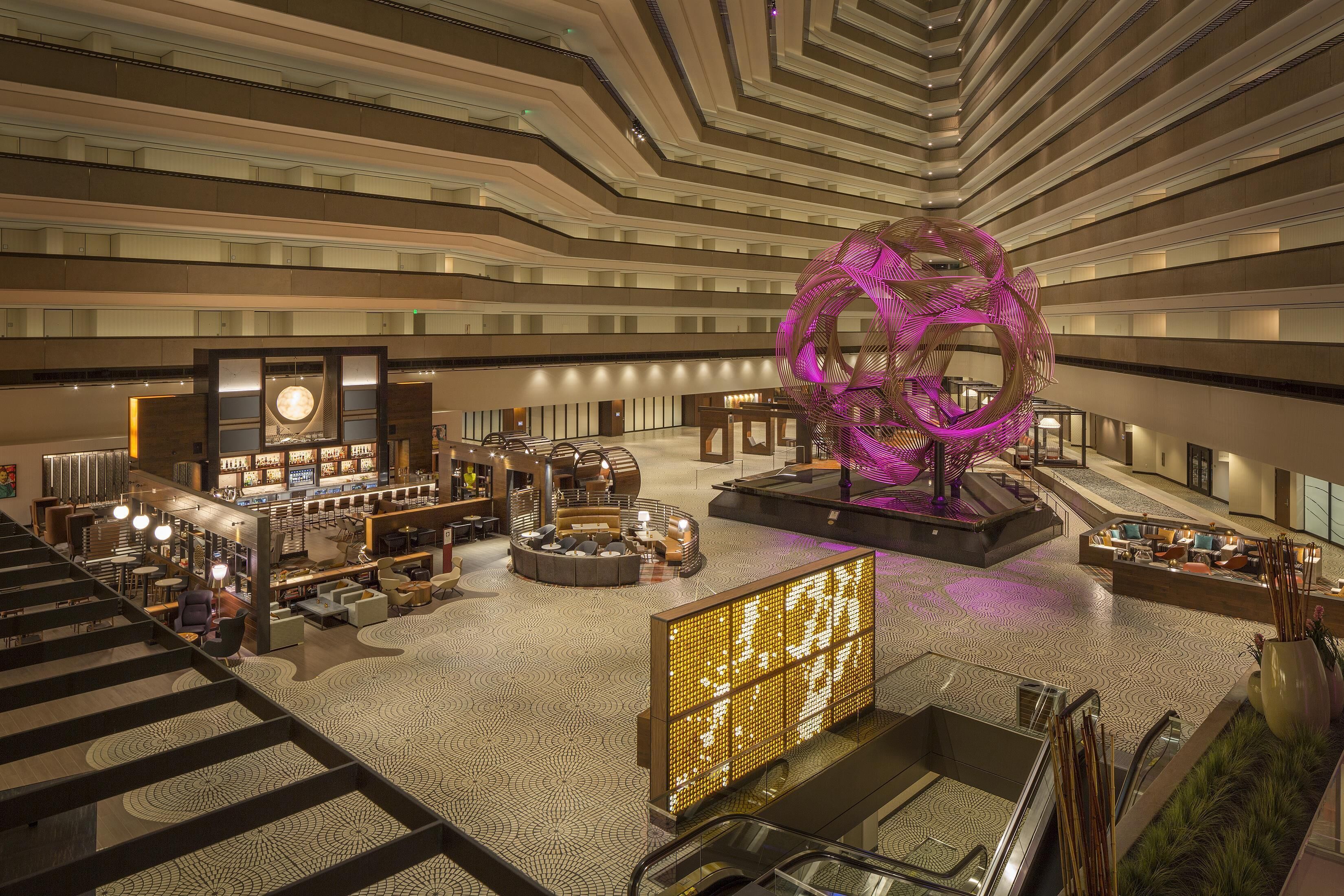 A modern hotel lobby with a central seating area, a large decorative sculpture, and a bar.