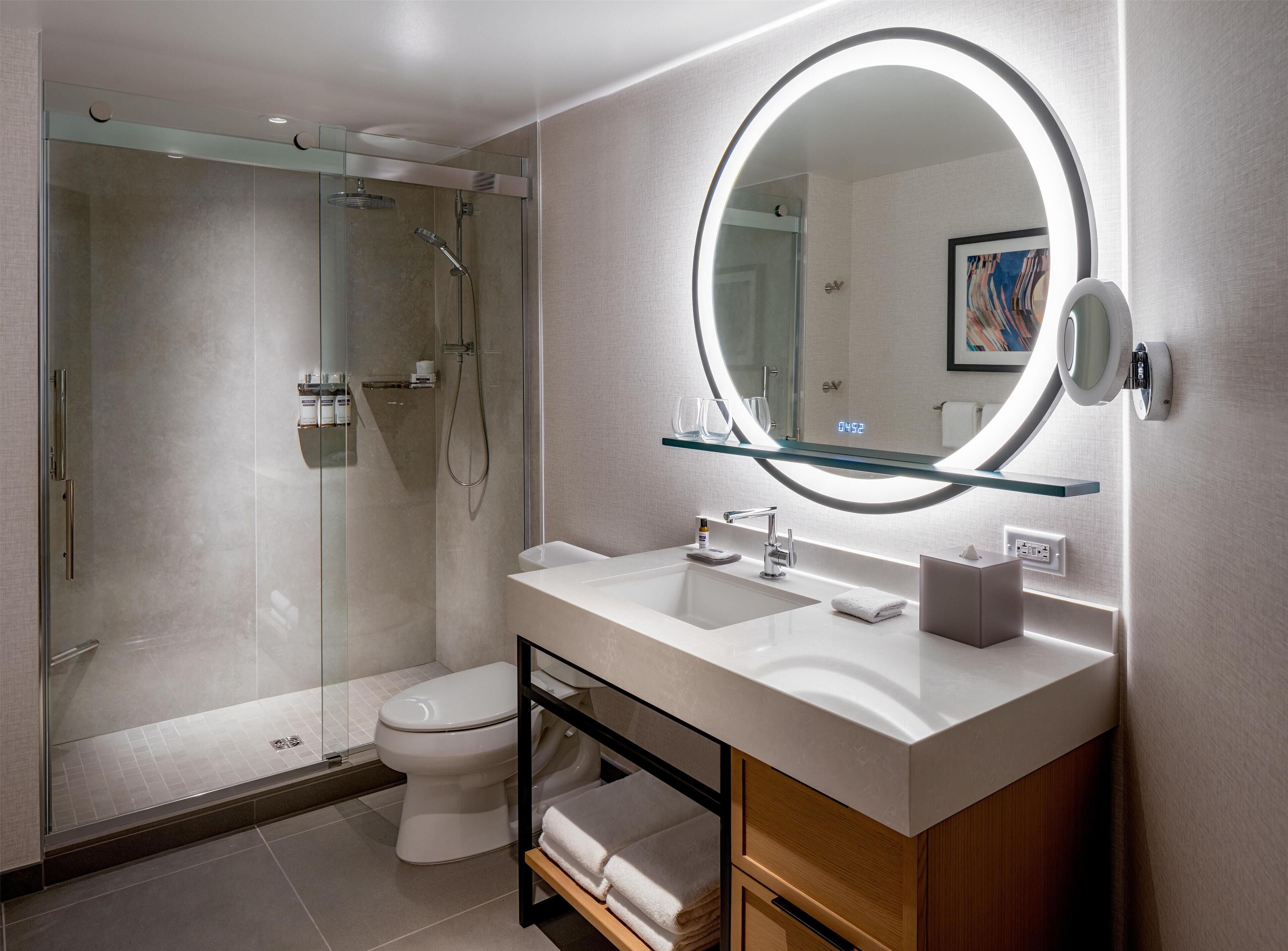 A modern bathroom with a glass-enclosed shower, a white sink with a mirror above it, and a towel rack.