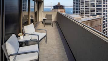 A balcony with two chairs and a small table, overlooking a cityscape and a bridge.