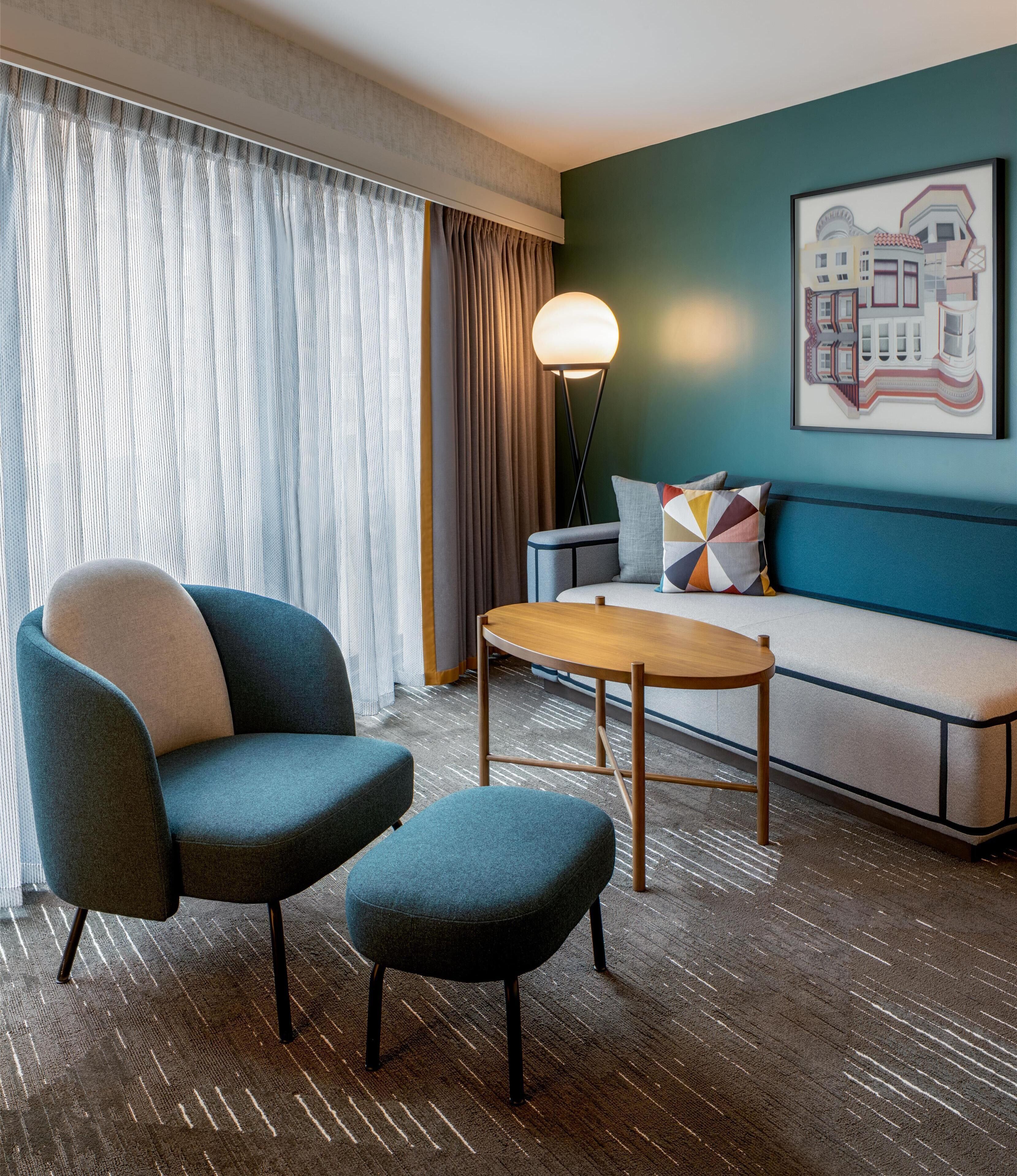 A modern hotel room with a sofa, two armchairs, a coffee table, and a floor lamp.