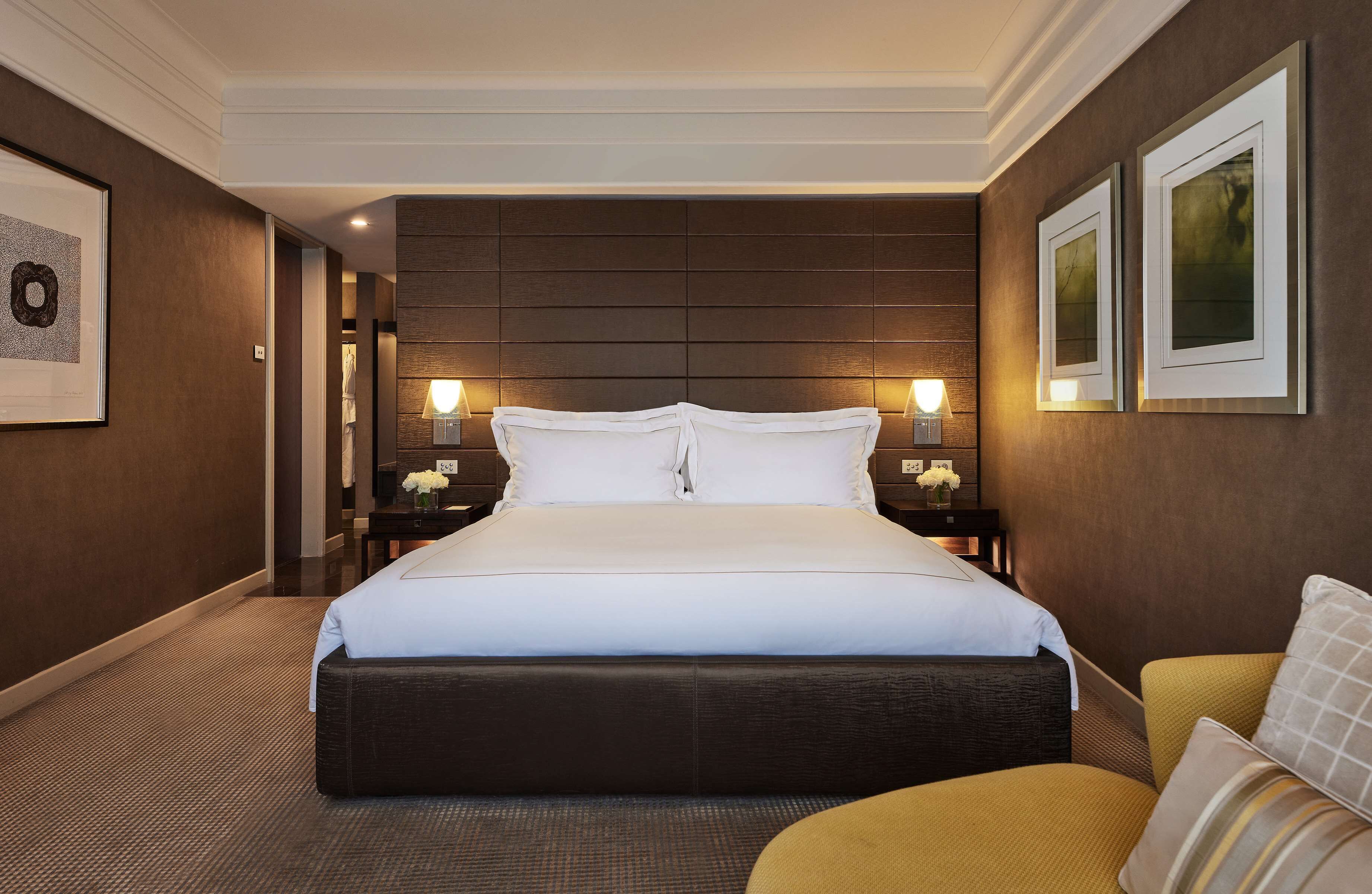 Una habitación de hotel con una cama grande, una mesita de noche, una silla y cuadros en las paredes.