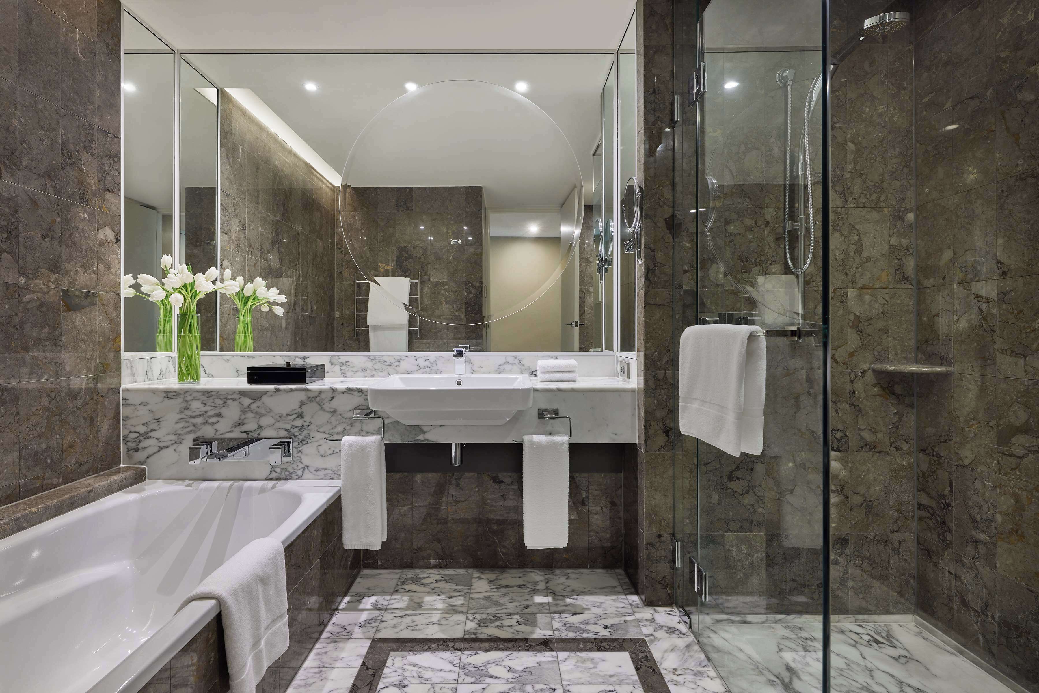 A modern bathroom with a glass-enclosed shower, a bathtub, and a vanity with a sink and mirror.