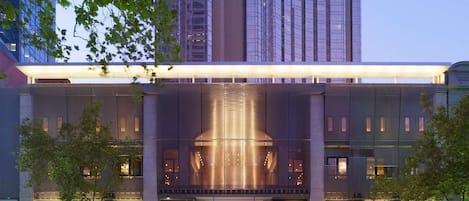 A modern hotel with a prominent glass facade, a grand entrance, and luxury brand signage.