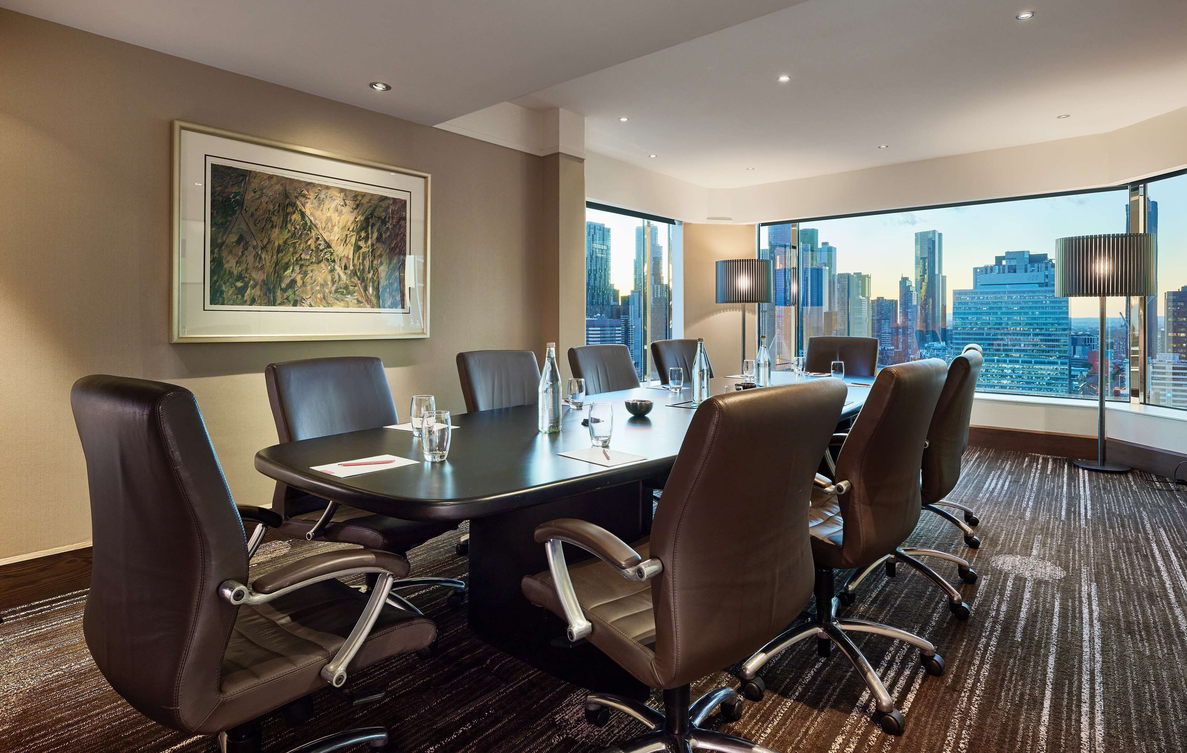 Un salón de conferencias con una gran mesa, seis sillas y vistas a la ciudad.