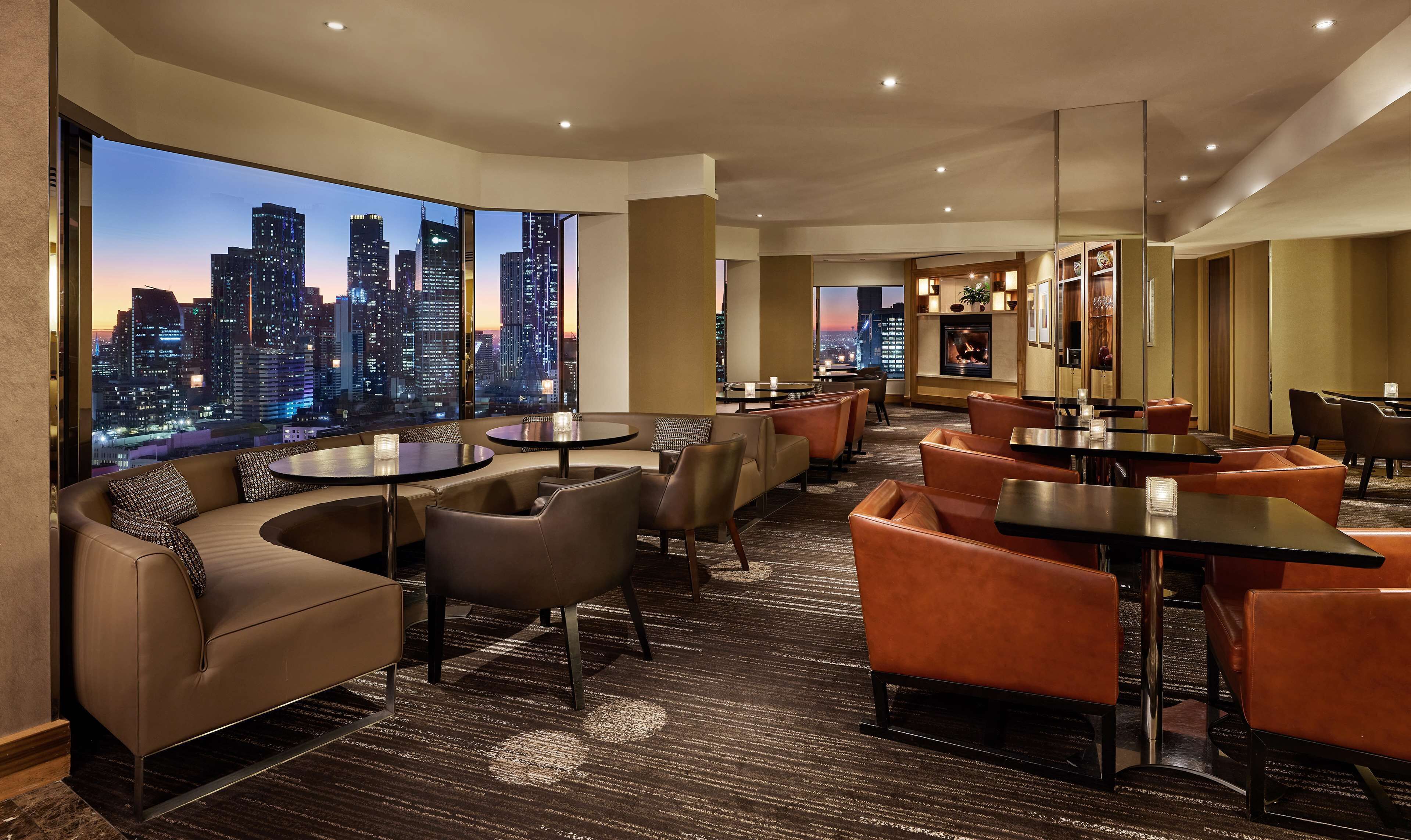 A modern hotel lobby with a city view, comfortable seating, and a fireplace.
