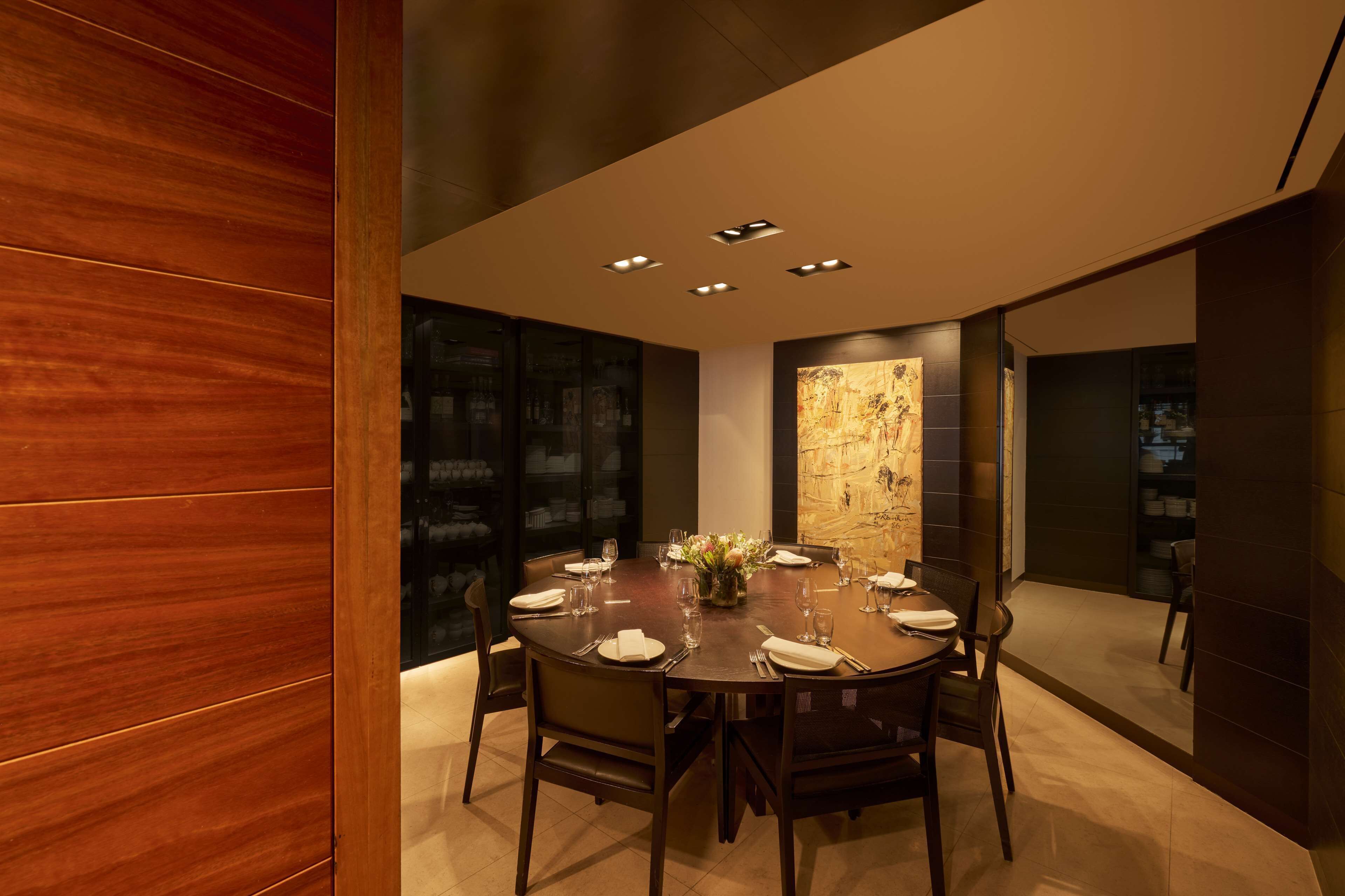 A modern dining area with a round table set for six, surrounded by dark wood chairs.