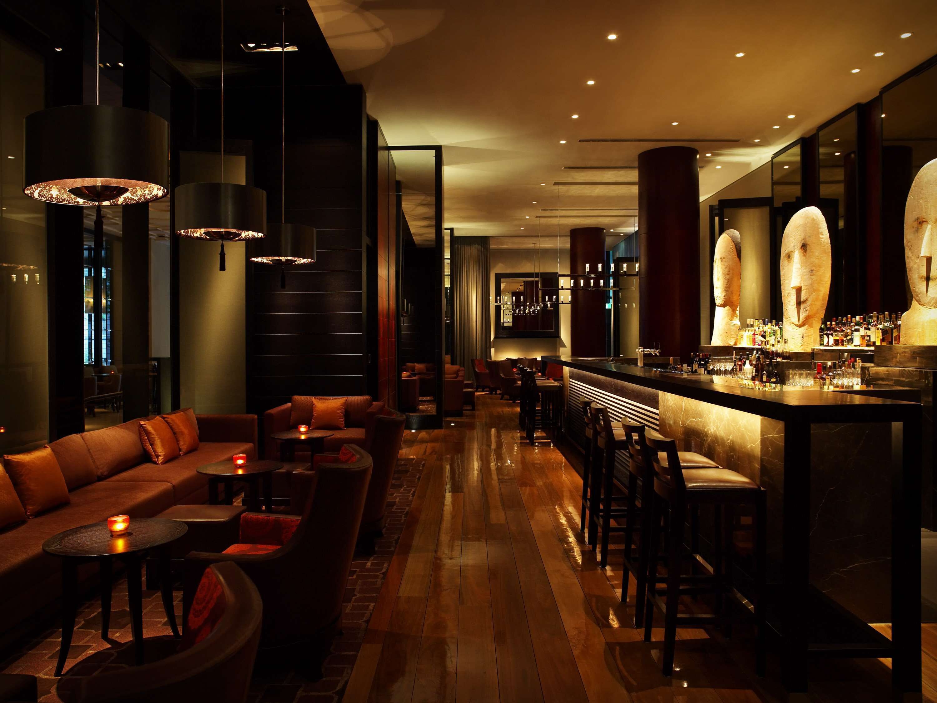 A modern bar area with a long counter, bar stools, and a seating area with a sofa and tables.