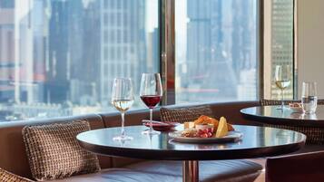 A dining area with a city view, featuring two round tables, each with a wine glass and a plate of food.