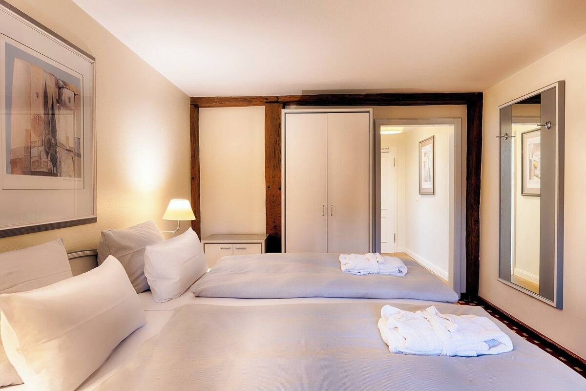 A hotel room with two beds, a bedside table with a lamp, a wardrobe, and a mirror.