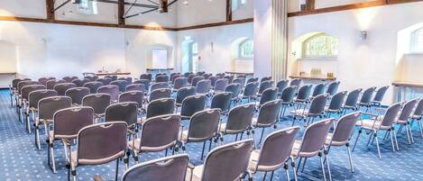 A conference room with rows of chairs, a stage with a podium, and large windows.