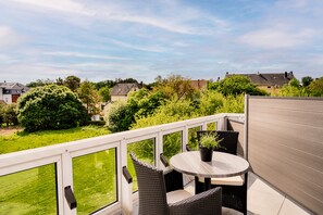 A balcony with wicker furniture, a round table, and a view of a green landscape and houses.