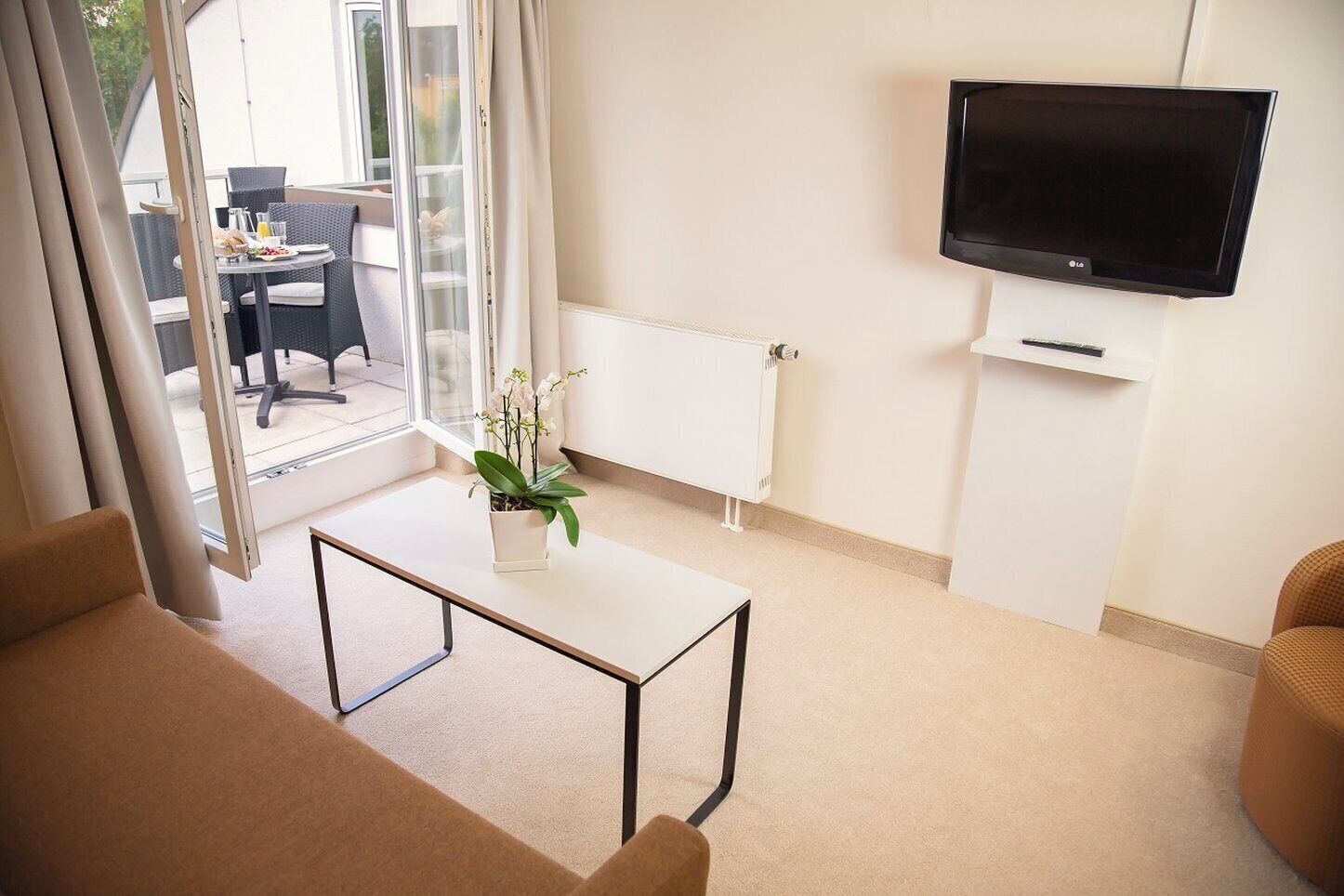 Una sala de estar moderna con un televisor de pantalla plana, un radiador blanco y una orquídea en maceta sobre una mesa blanca.